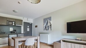 Una cucina moderna con microonde, macchina del caffè e frigorifero. È presente una zona pranzo con tavolo e sedie. Un grande televisore a schermo piatto è fissato al muro.