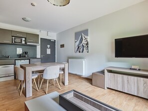Eine moderne Küche mit Mikrowelle, Kaffeemaschine und Kühlschrank. Es gibt einen Essbereich mit Tisch und Stühlen. Ein großer Flachbildfernseher ist an der Wand montiert.
