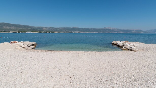 Una spiaggia con ciottoli, acque cristalline e affioramenti rocciosi.