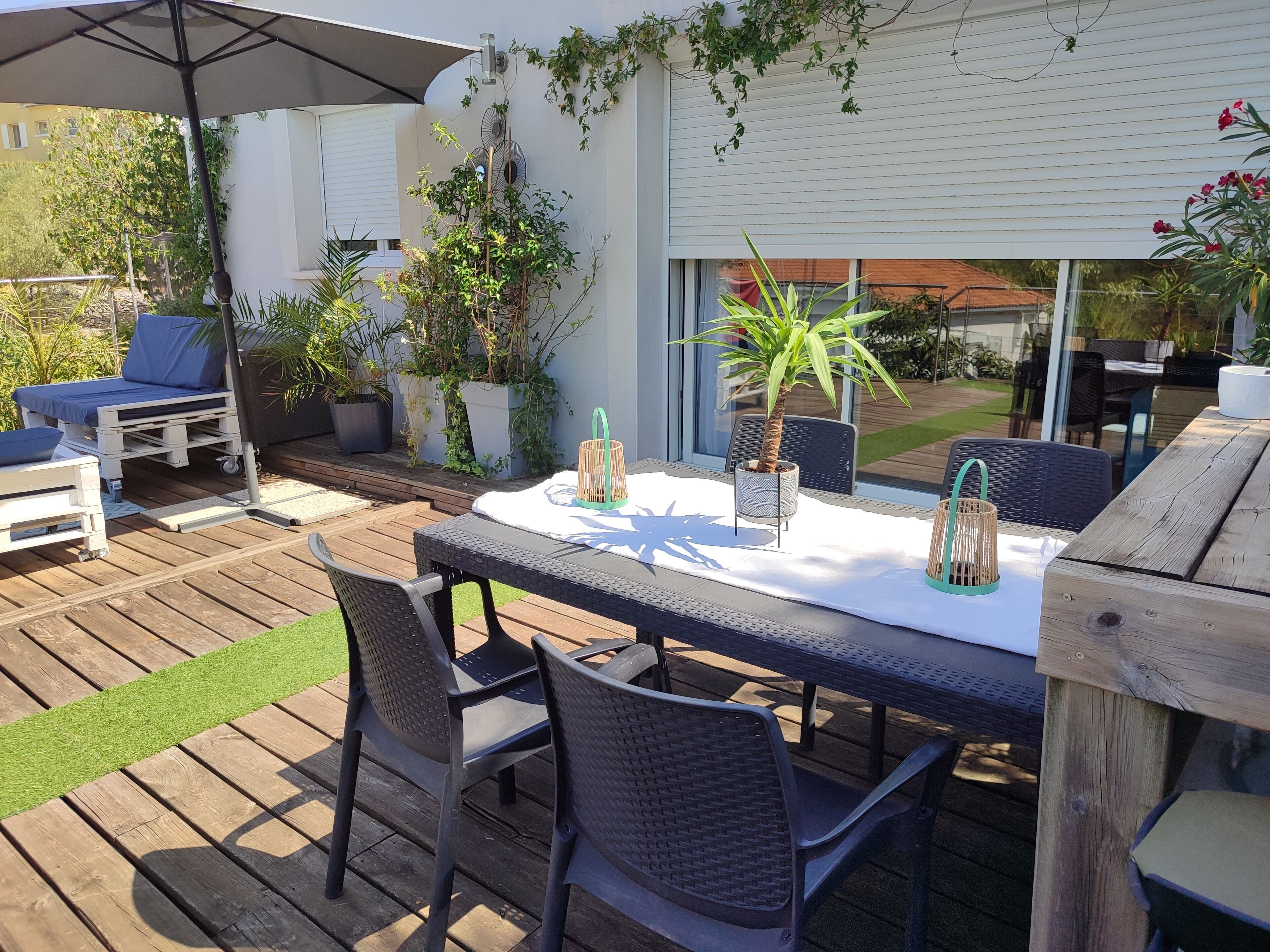 An outdoor patio with a wooden deck, a round table with chairs, a blue lounge chair, and potted plants.