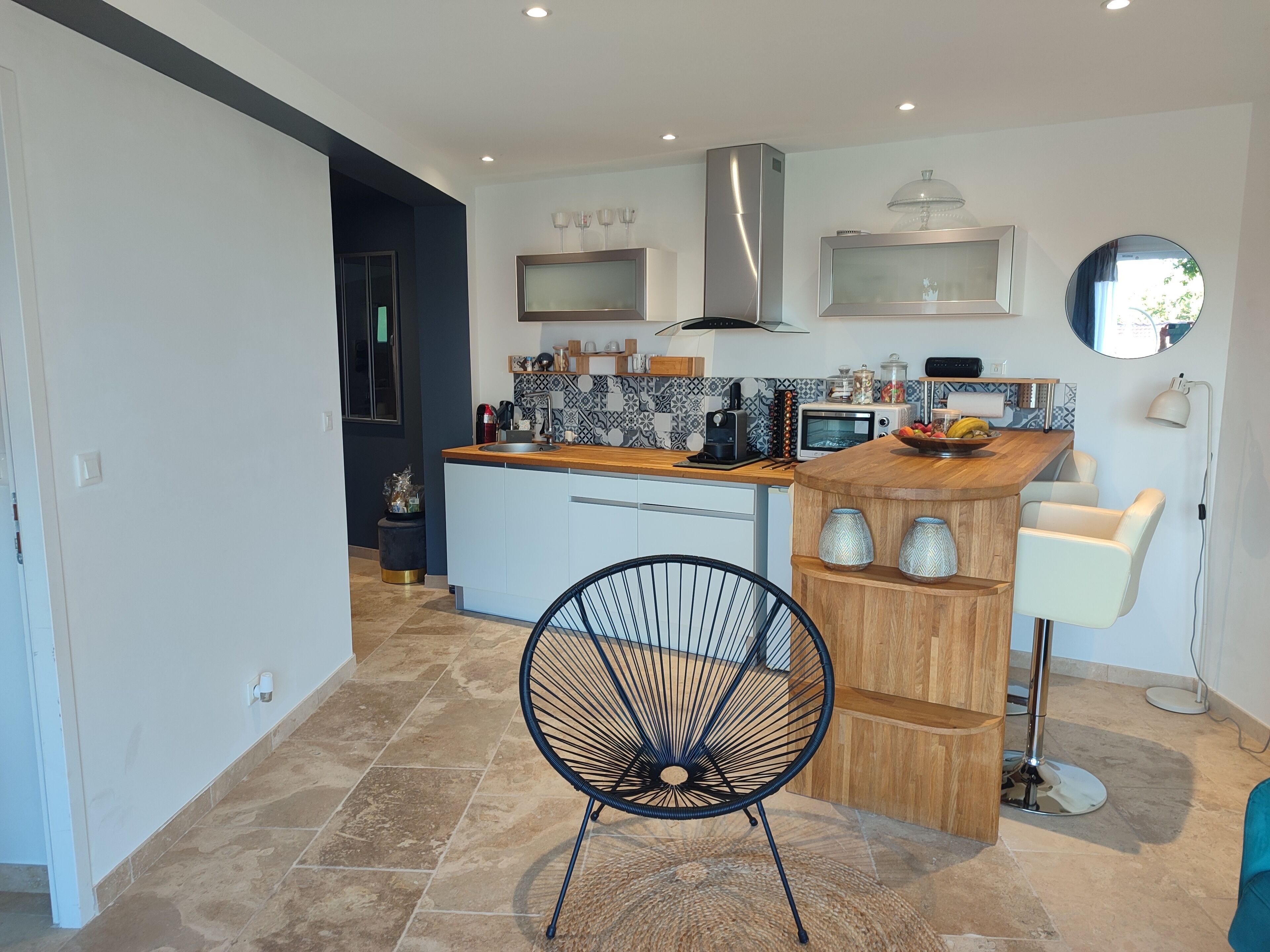 Une cuisine moderne avec un îlot central, un coin repas avec une chaise et un grand miroir au mur.