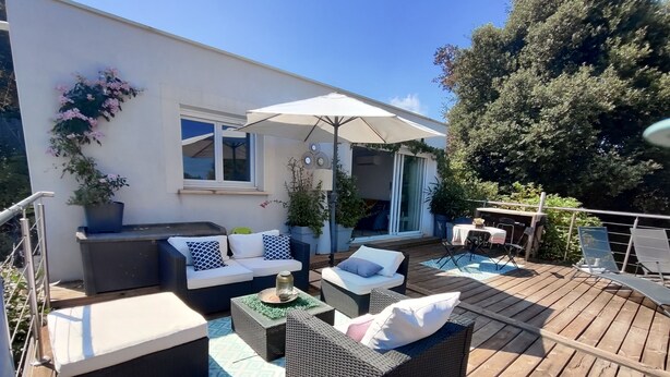 Eine Holzterrasse mit Gartenmöbeln, darunter Sofas und ein Tisch, und ein großer Sonnenschirm, der Schatten spendet.