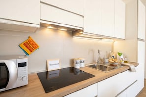Eine moderne Küche mit Mikrowelle, Induktionskochfeld und Spüle aus Edelstahl. Zwei Gläser mit der Aufschrift 'SALUGA' sowie ein kleines Schild mit einer Website-Adresse sind vorhanden.