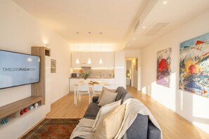 A modern living room with a flat-screen TV, a sofa, a dining area, and a kitchen in the background. - Sea Breeze Suite – Your Haven of Light and Comfort (Bari)