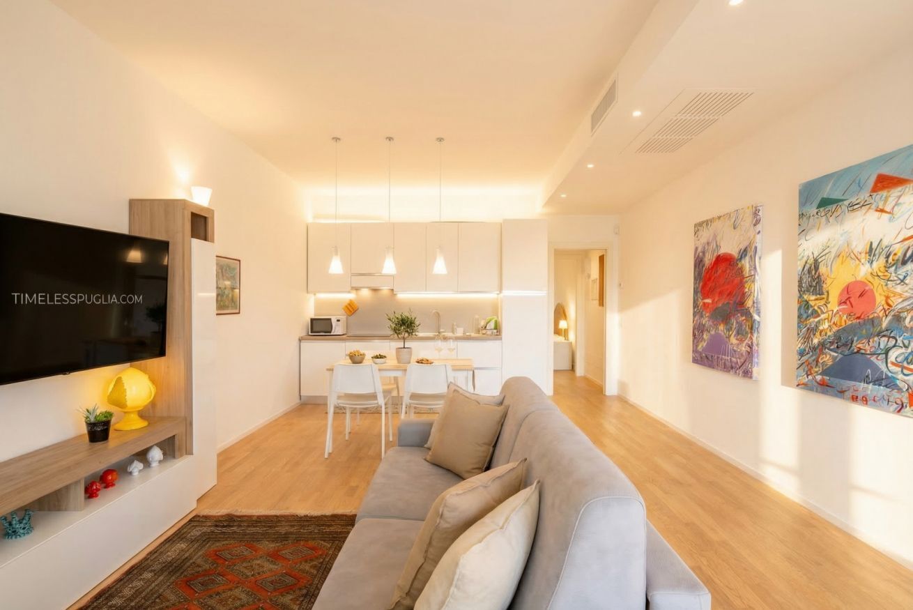 Ein modernes Wohnzimmer mit Flachbildfernseher, einer Couch, einem Essbereich und einer Küche im Hintergrund.