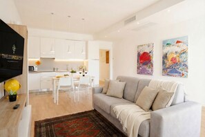 Ein modernes Wohnzimmer mit grauem Sofa, Fernseher und Essbereich mit weißen Möbeln.