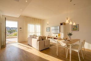 Ein modernes Wohnzimmer mit Sofa, Esstisch, Stühlen, Fernseher und einem Balkon mit Blick.