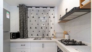 A modern kitchen with white cabinets, a stainless steel sink, a gas stove, and a microwave. - Alba Gardens B1102 (Nairobi)