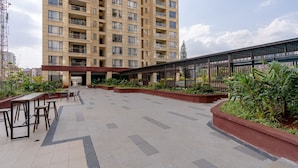 A spacious outdoor area with a high-rise building in the background, featuring a covered walkway and seating areas. - Alba Gardens B1102 (Nairobi)