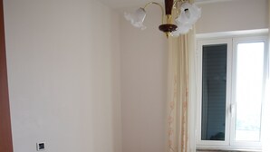 A bedroom with two beds, a wooden dresser, a nightstand, a lamp, and a window with curtains. - Valley vacation home (Locorotondo)