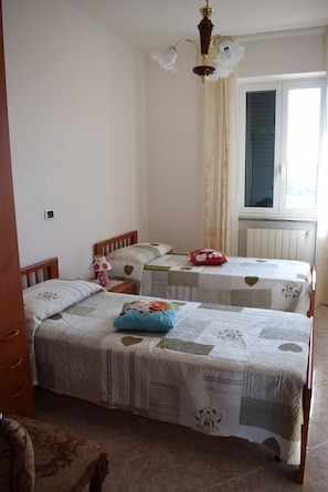 Ein Schlafzimmer mit zwei Betten, einer Holzkommode, einem Nachttisch, einer Lampe und einem Fenster mit Vorhängen.