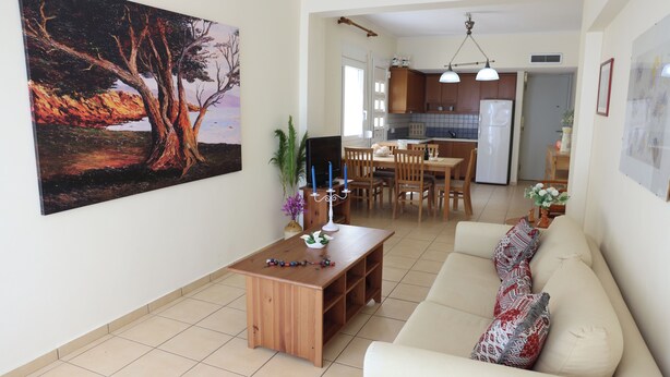 A living room with a wooden coffee table, a beige sofa with patterned cushions, and a painting on the wall. - Entire home in Lilikas, Greece (Kalamoti)
