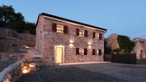 Un edificio in pietra con una porta e finestre, circondato da un vialetto sterrato e mura di pietra.