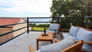 Un balcone con un muro in pietra, un tavolo di legno e due sedie di legno con cuscini grigio chiaro.