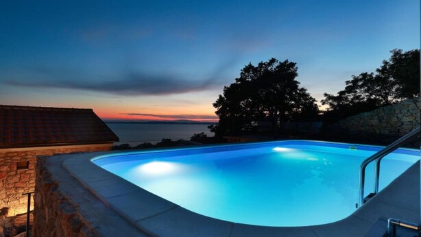 Una piscina con una parete in pietra e vista sul tramonto sull'acqua.