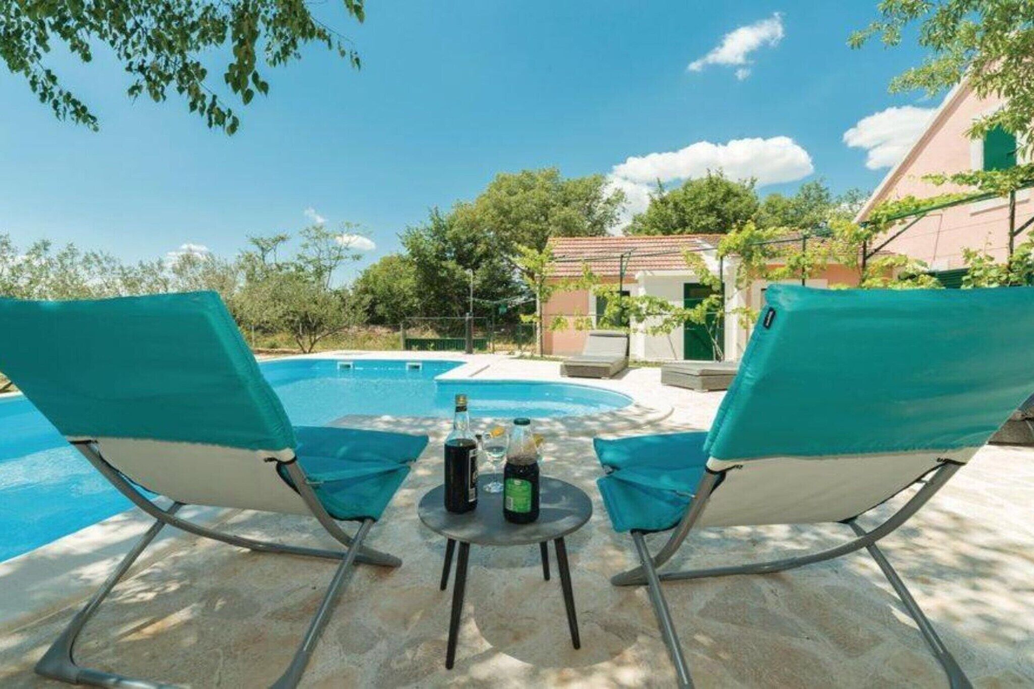 A poolside area with two lounge chairs and a table with bottles.