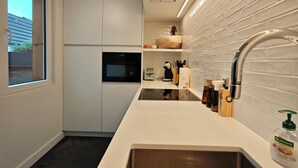 A modern kitchen with a stainless steel sink, white cabinets, a built-in oven, and a window. - Cozy, quiet apartment 200 meters from the sea with garage (Middelkerke)
