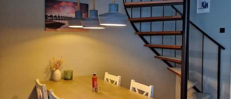 Un'area pranzo con un tavolo in legno e sedie bianche, un quadro appeso al muro e una scala a chiocciola.