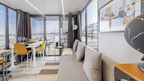 A modern hotel room with a balcony, a dining area, and a sofa. - The Homeboat Company - PDN (Lisboa)
