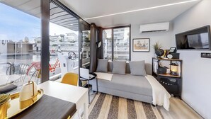 A modern living room with a sofa, a dining table, and a TV. - The Homeboat Company - PDN (Lisboa)