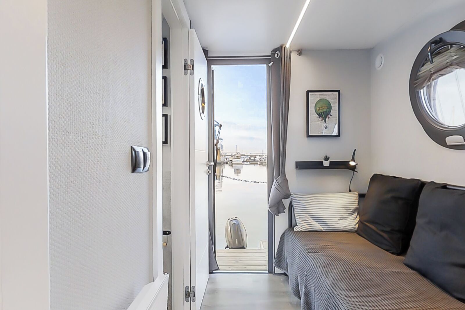 A compact, modern interior with a bed, a small seating area, and a view through a door to an outdoor area.
