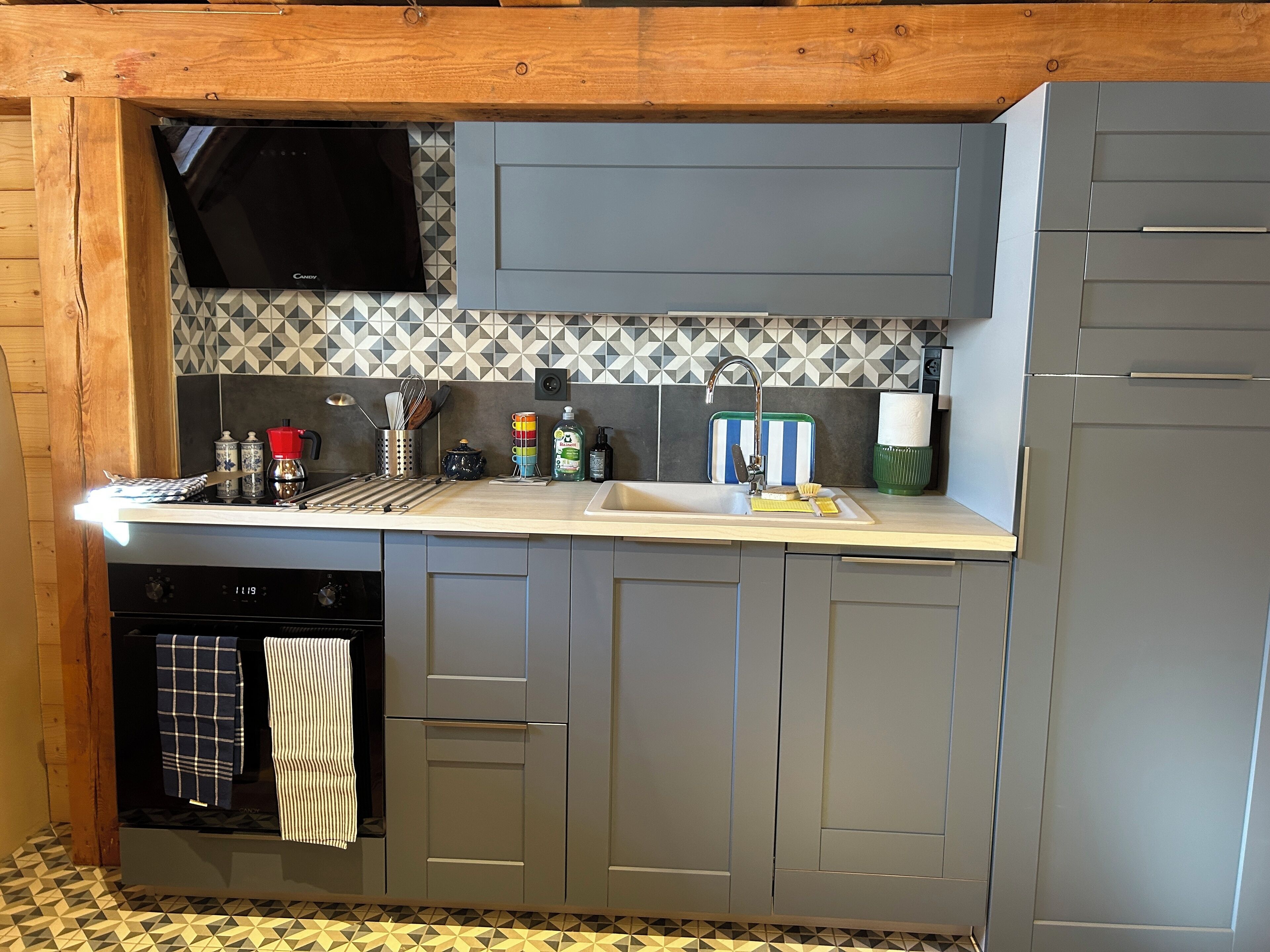 Een moderne keuken met grijze kastjes, een betegelde spatwand en een inbouwoven.