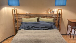 Een bed met een houten hoofdbord, twee bedlampjes en een klein tafeltje ernaast.