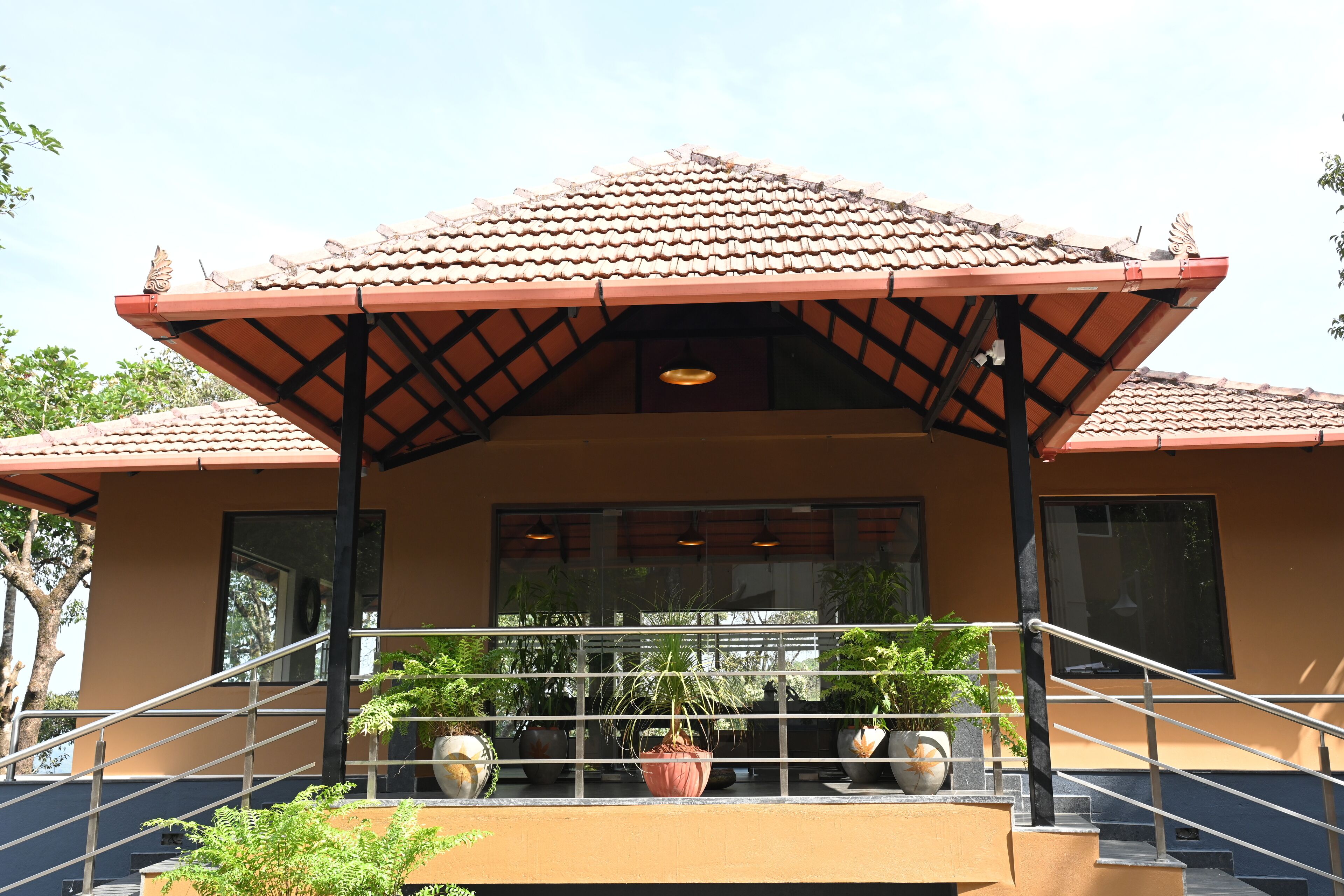 A building with a tiled roof, a covered entrance with a railing, and potted plants.