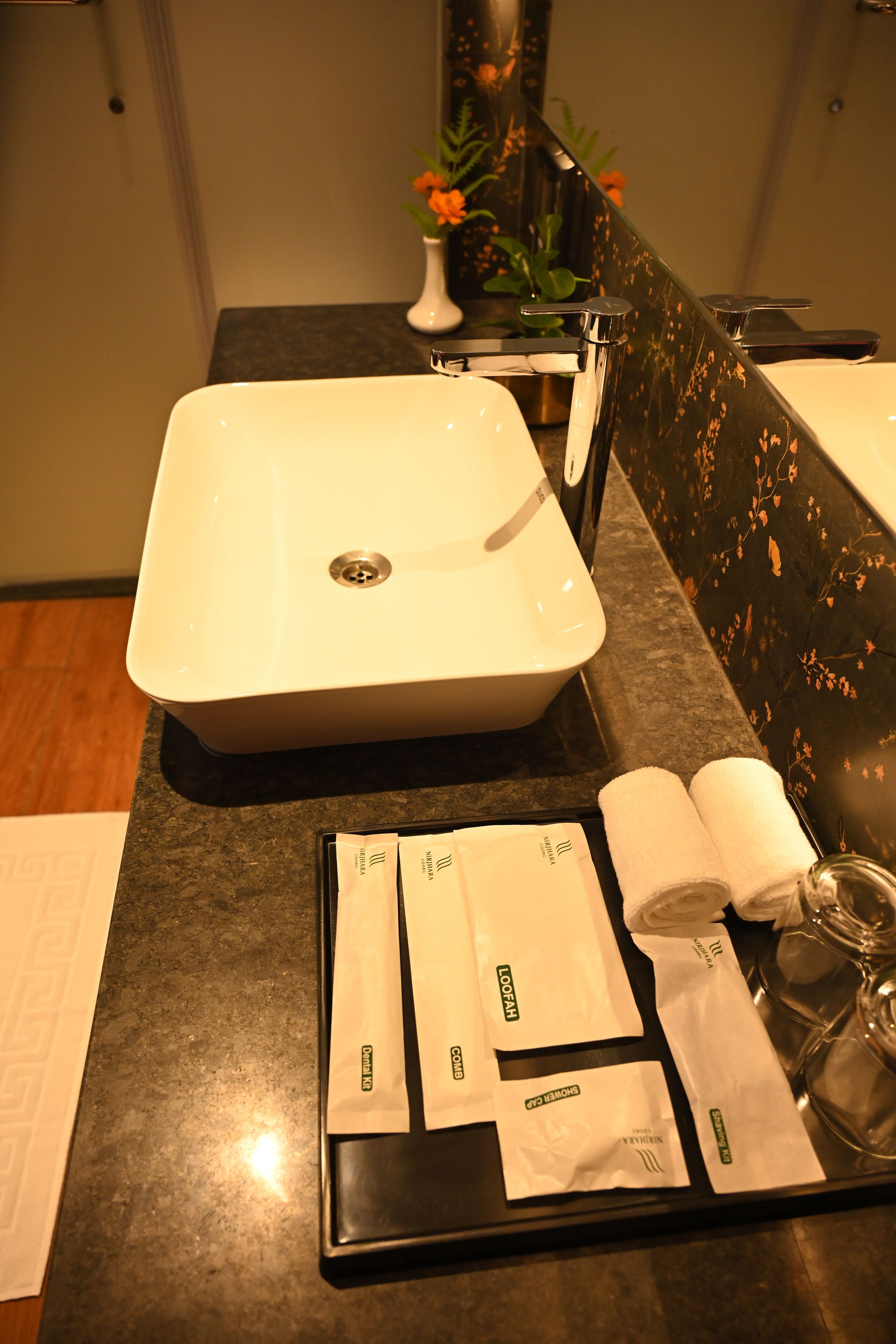 A bathroom with a white sink, a black countertop, and toiletries on a tray.