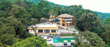 A multi-story hotel with a pool and lush surrounding forest.