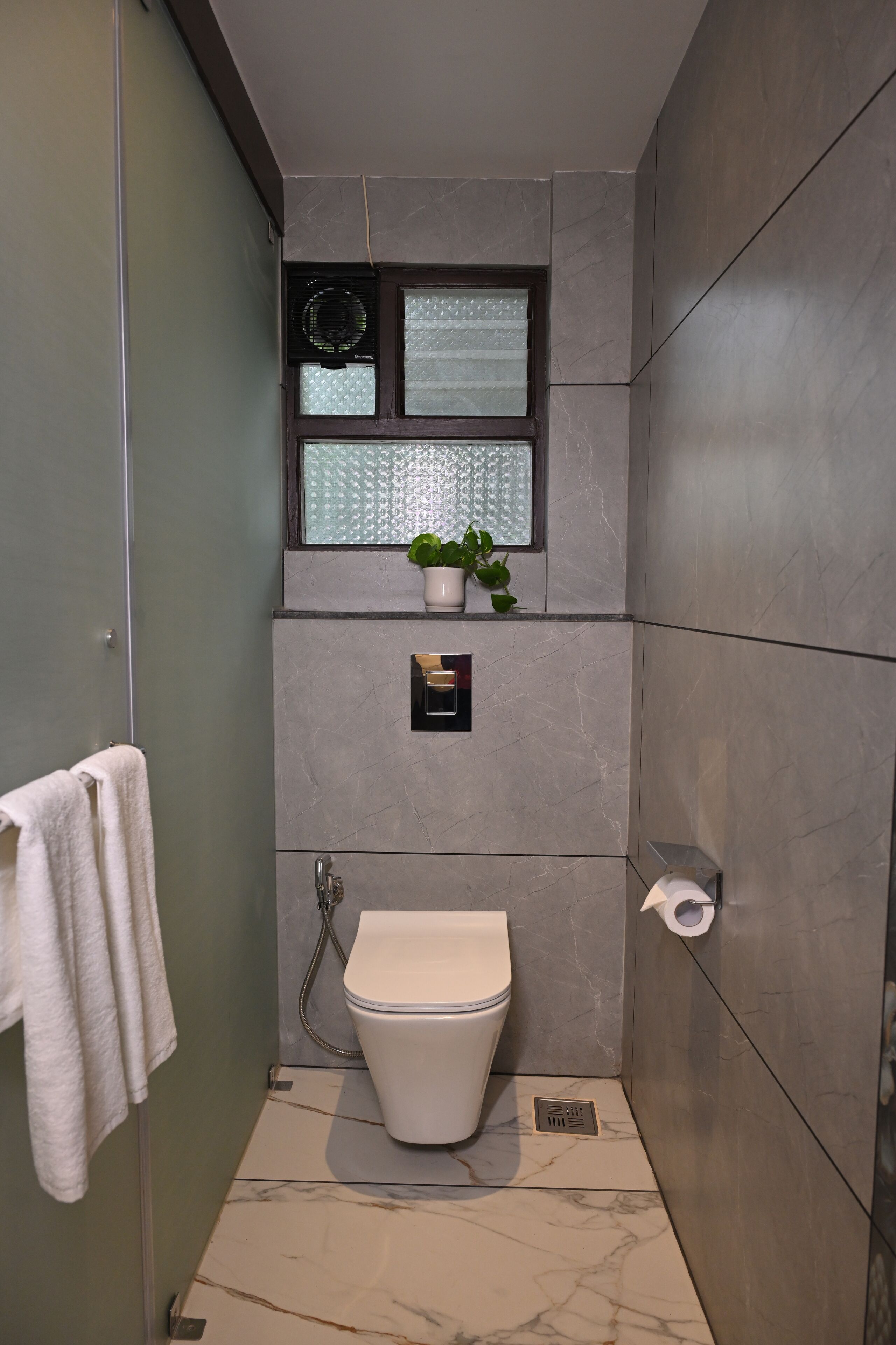 A modern bathroom with a toilet, a shower, and a window with a plant.