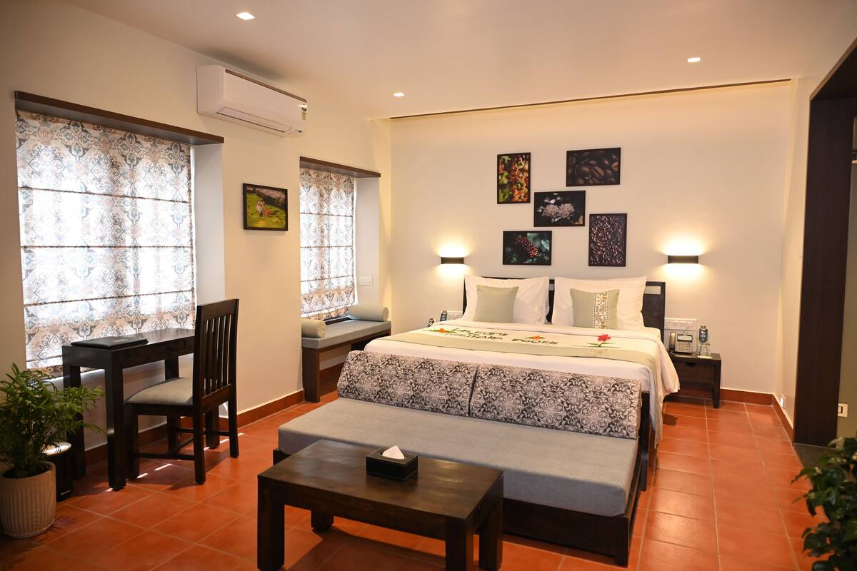 A hotel room with a bed, bedside tables, a chair, a small table, and a potted plant.