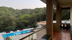 A balcony with a pool, lounge chairs, and a view of a forested hillside. - Nirjhara Coorg  (Somvarpet)