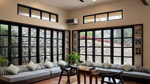 A spacious room with large windows, a central seating area with a chessboard, and a stone wall backdrop. - Nirjhara Coorg  (Somvarpet)