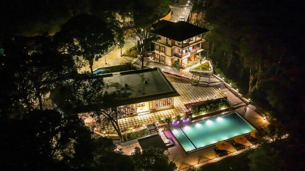 A two-story building with a swimming pool, outdoor seating, and a well-lit patio area. - Nirjhara Coorg  (Somvarpet)