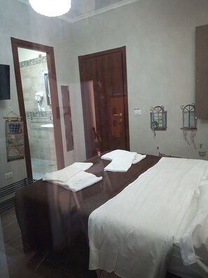 Une chambre d’hôtel avec deux lits, une porte en bois, un miroir et une petite fenêtre avec des volets.