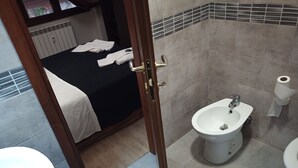 Et badeværelse med bidét, toilet og et håndklædestativ med håndklæder.