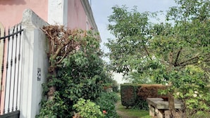 A garden with a pathway leading to a building with a pink facade and a flag. - Charming farmhouse for rent (Riachos)