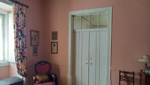 A room with a pink wall, a white door, a wooden chair, a bench, and a small table. - Charming farmhouse for rent (Riachos)