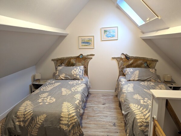 A small, cozy attic bedroom with two single beds, wooden flooring, and a sloped ceiling with skylights.