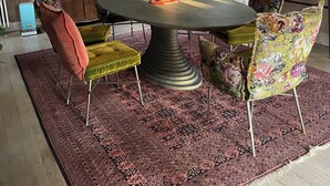 A dining area with a round table, floral chairs, a patterned rug, and a cabinet with decorative items. - Régine MAUFFREY (Champagney)