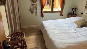 A bedroom with a bed, wooden floor, curtains, a ceiling fan, and a window with curtains. - Wooden house, côte landaise 5min ocean, lakes, ideal family, animals accepted! (Biscarrosse)