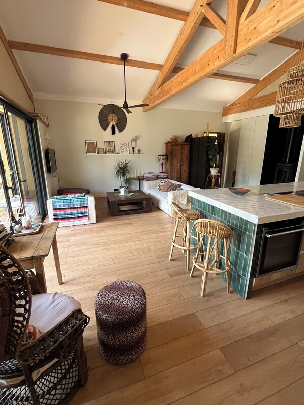A spacious kitchen with wooden beams, a dining area with a table and chairs, and a cozy seating area with a patterned ottoman. - Wooden house on the Landaise Coast, 5 minutes from the ocean and lakes; ideal for families; pets allowed! (Biscarrosse)