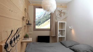 A bedroom with a bed, a hanging chair, a white wall shelf, and a view of a mountainous landscape through a window.
