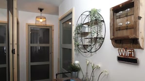 A hallway with a wooden bench, a wall-mounted WiFi sign, a metal shelf with plants, and a door with frosted glass panels.