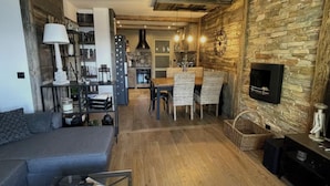 A modern living room with a sofa, a dining area with a table and chairs, a fireplace, and a kitchen in the background.