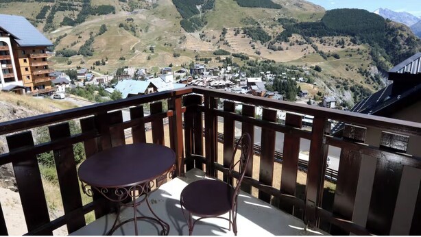 A balcony with a table and chairs, overlooking a town and mountains.