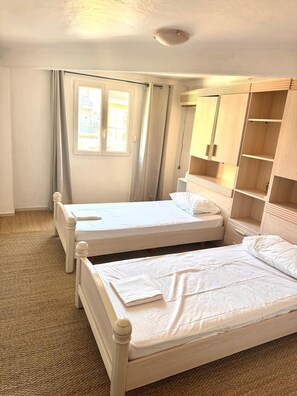 Ein Zimmer mit zwei Einzelbetten, einem Holzschrank, einem Fenster mit Vorhängen und einer Deckenleuchte.