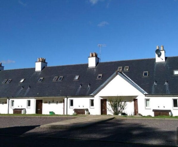 A row of white buildings with dark roofs and multiple chimneys, featuring a central entrance with a white facade.