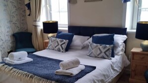A neatly made bed with a blue throw blanket and pillows, a bedside table with a lamp, and a window with curtains. - Portsonachan Hotel (Dalmally)